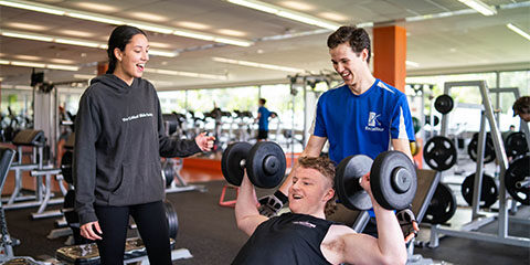 Male student holds dumb bells while a male and female student talk to him