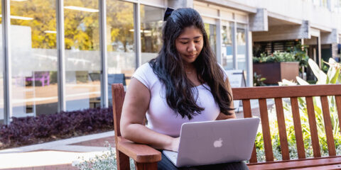 girl sitting on a bench outside and looking at her laptop