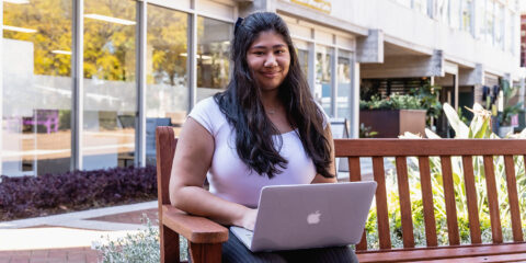 female student sitting on an outside bench and on her laptop