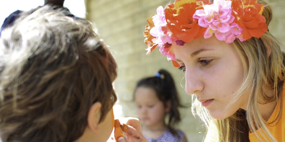 Lady wearing a flower crown, painting the face of a child