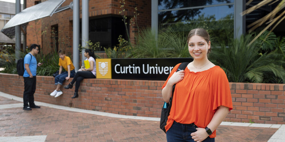 Woman standing in foreground in front of Curtin sign, with three people talking in background