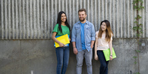 Three people standing in front of wall together smiling