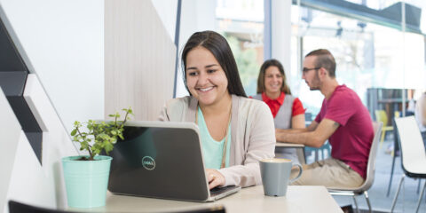Lady on laptop with two people in background sitting