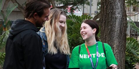 Two people talking to a lady in a green mentor shirt
