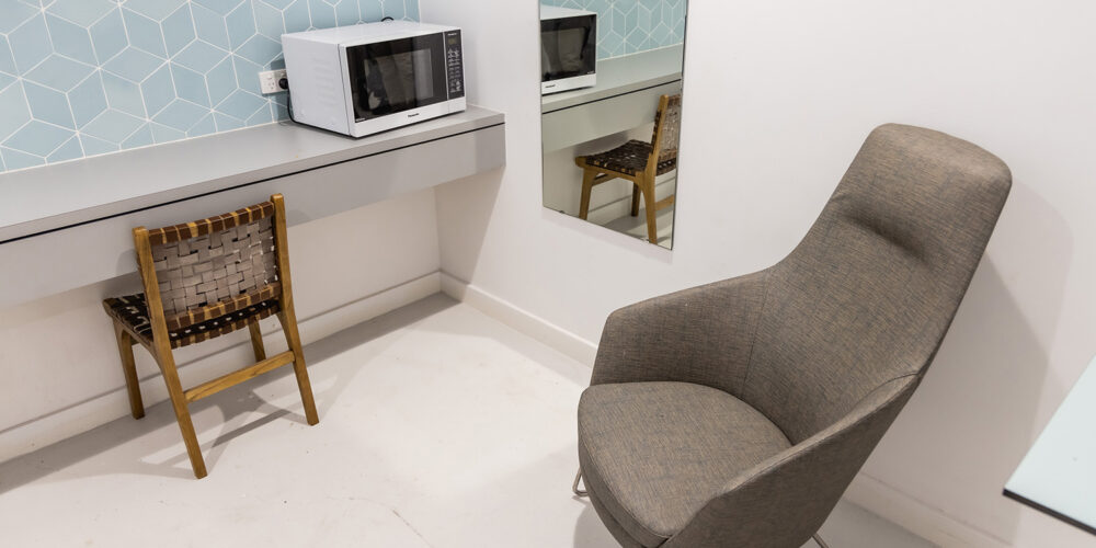 Curtin Perth's nursing room. A large, empty, chair is placed on the right, next to a mirror. A microwave is placed on top of a table. Another small chair is tucked under the table.  The microwave and small chair is situated on the left.