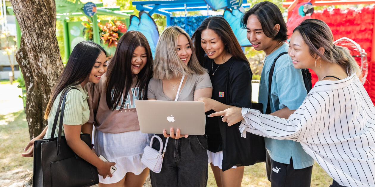Group of students smile looking at a laptop that one student is holding.