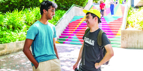 Two male students laughing next to a colorful staircase