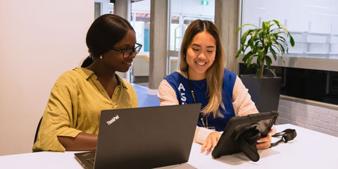 A student and a library helper sit at a desk smiling.