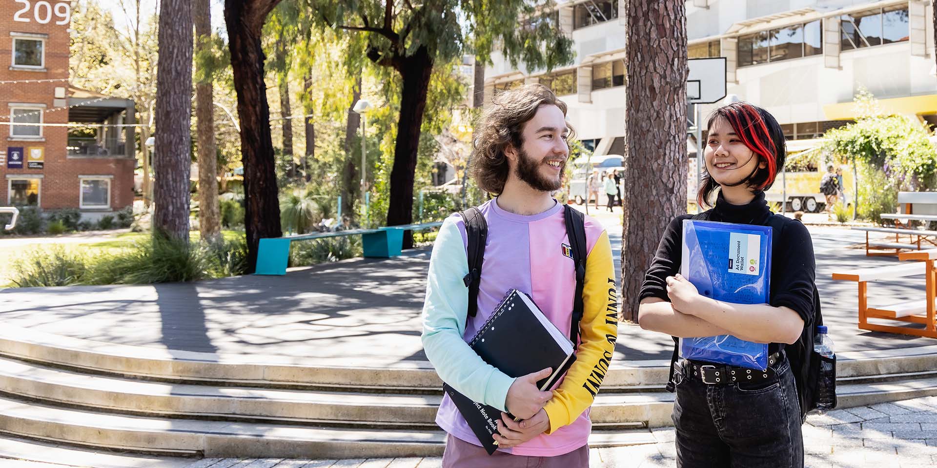 Two students are walking on campus holding textbooks in their hands.