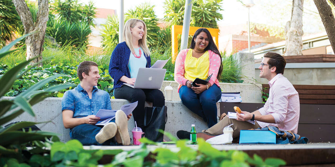 Four students sitting on a wall outside smiling and chatting.