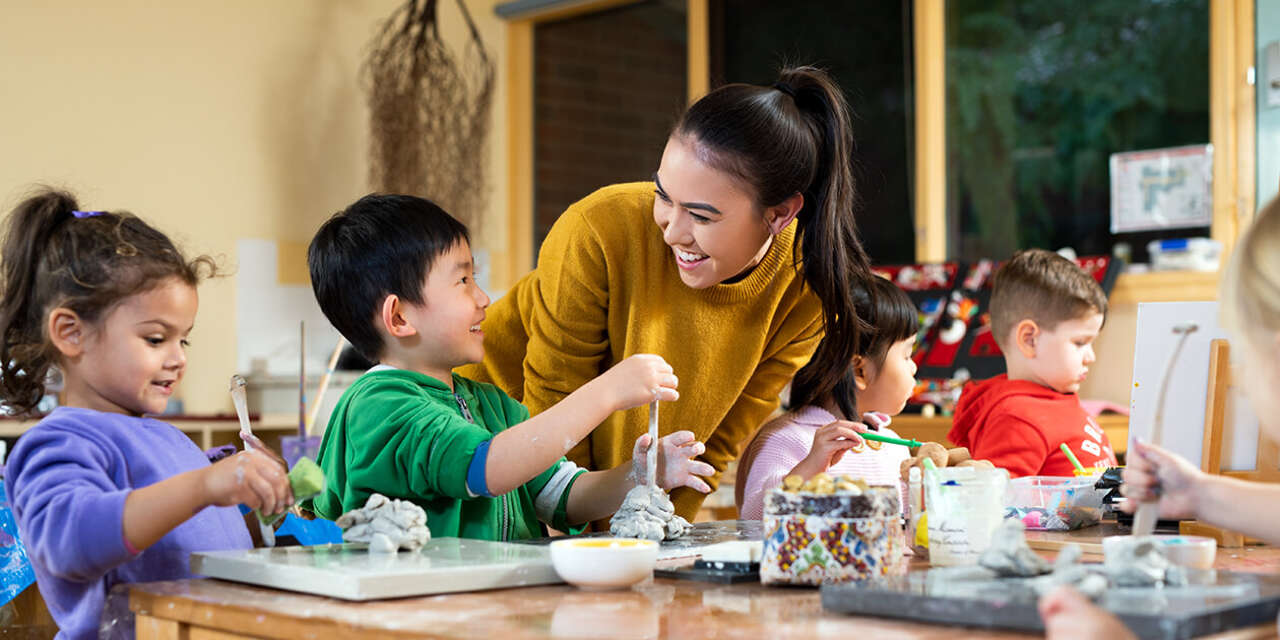 An educator smiling at three children completing an activity.