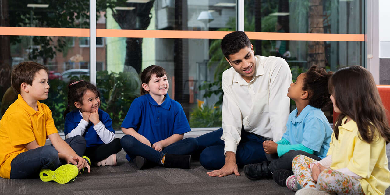 An educator sitting on the ground surrounded by primary-school agedchildren