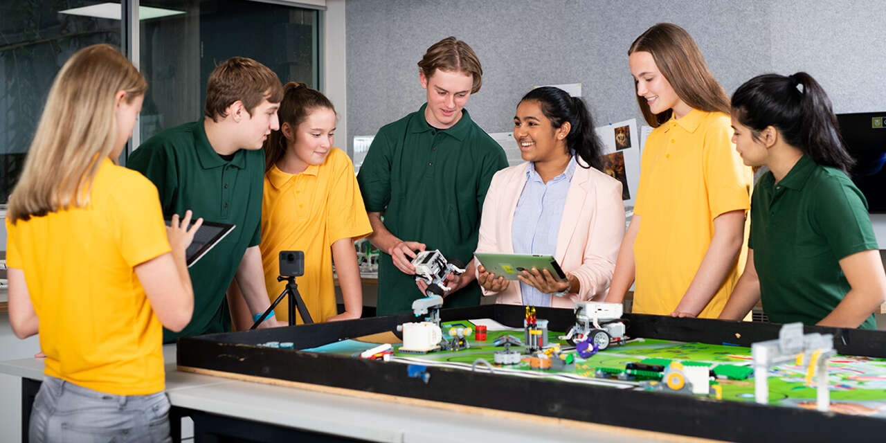 A smiling educator surrounded by secondary school students.