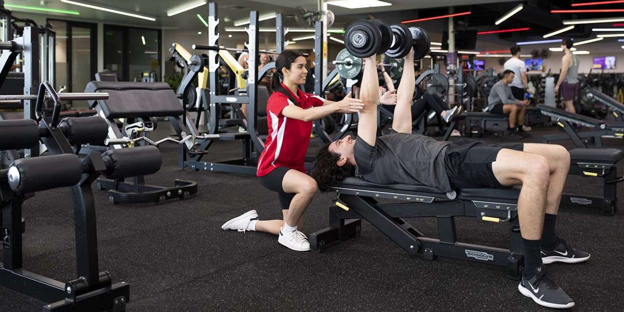 Young women supervising a male client doing weight exercises in a gym..