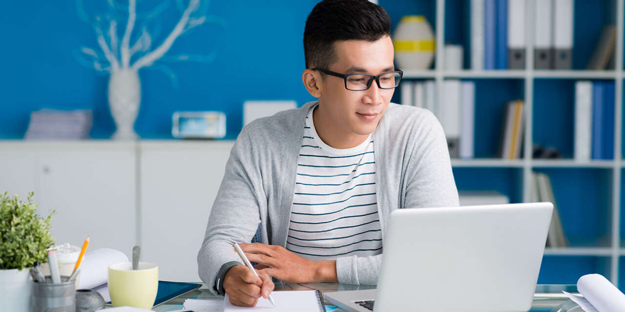 A student sits at a desk, studying on his laptop.