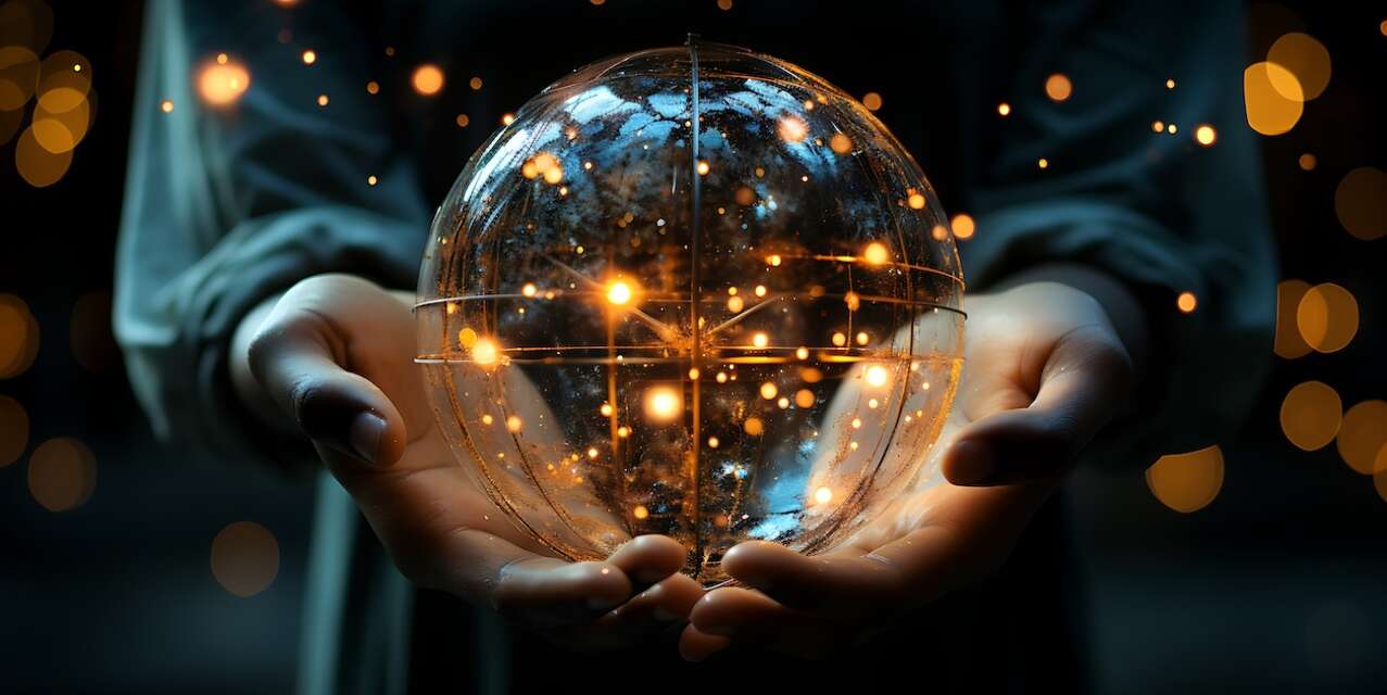 Close up of hands cupped around a clear sphere with lights glowing inside and around it.