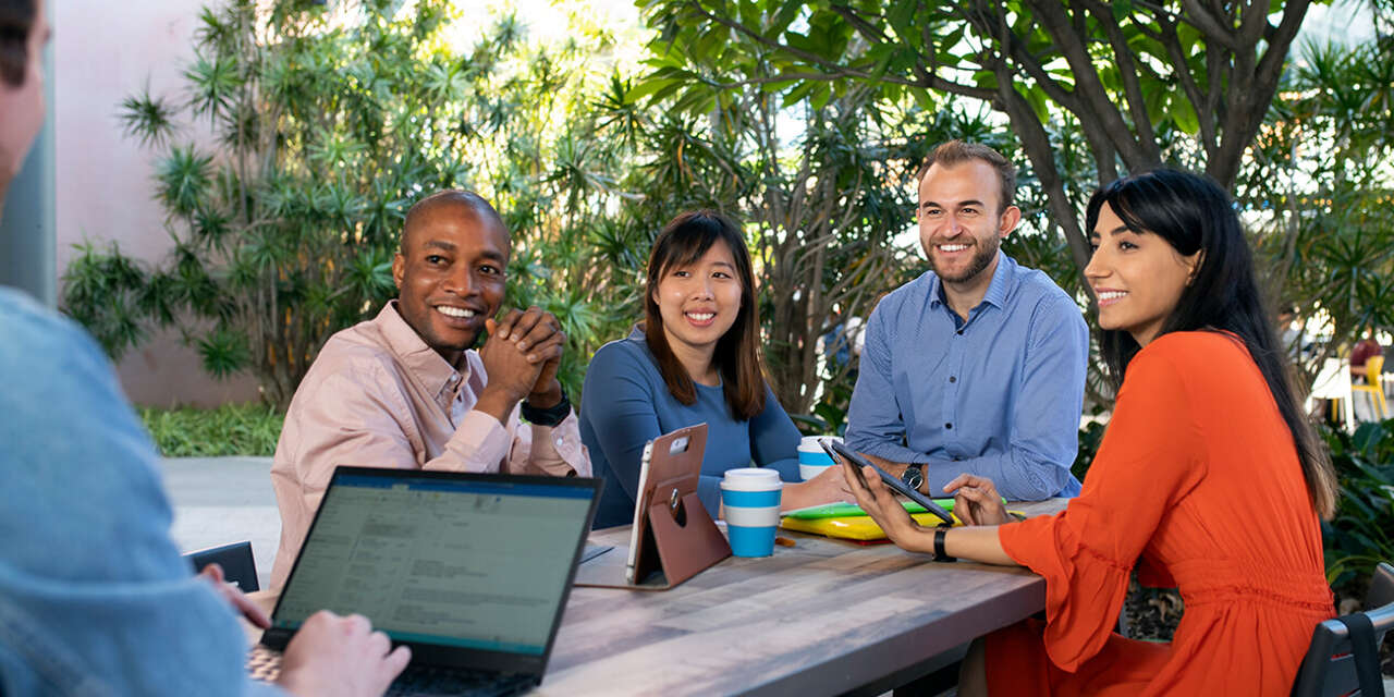 Group of Curtin students sitting together outdoors, laughing and studying with laptops and notes.