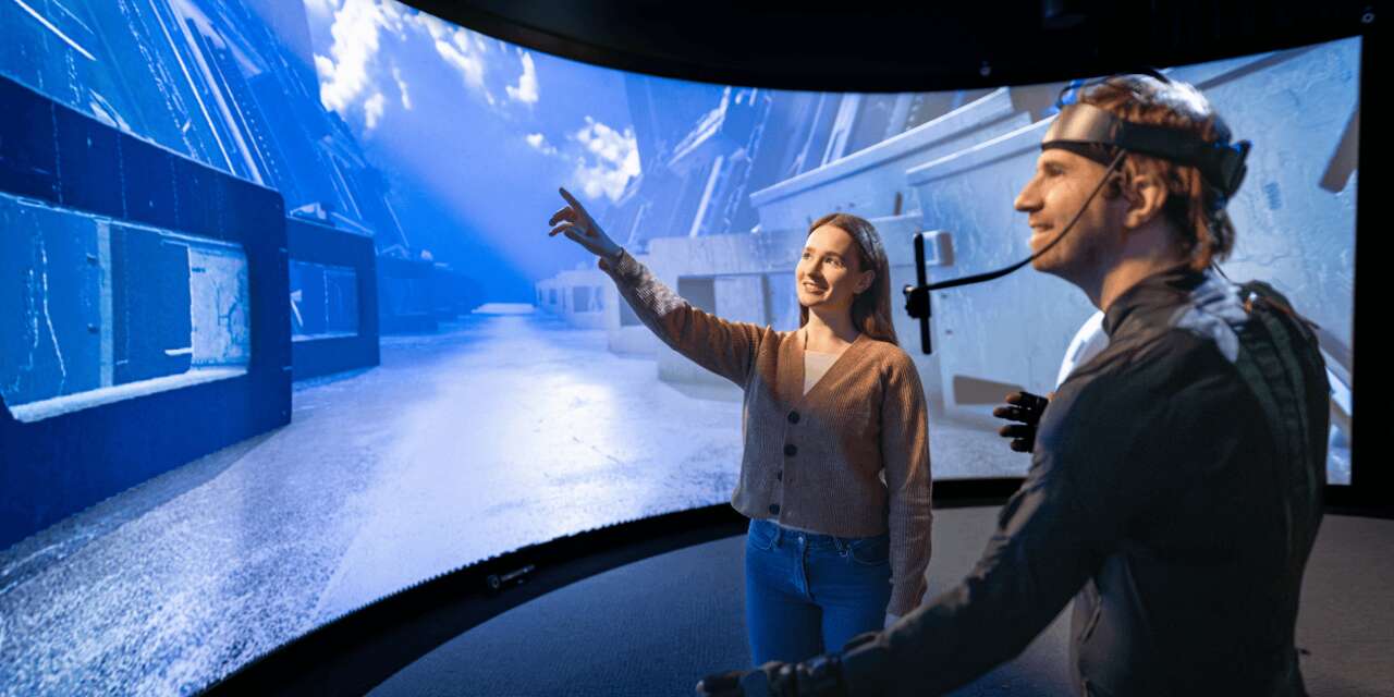 Two people smiling at a large blue screen showing an immersive experience.