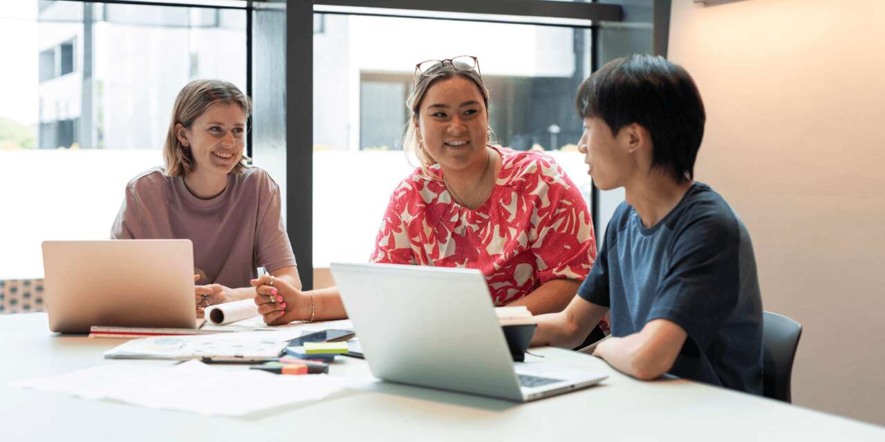 Three students working at a table and smiling