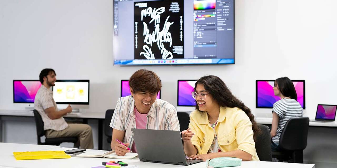 Two students laughing and looking at a computer screen together