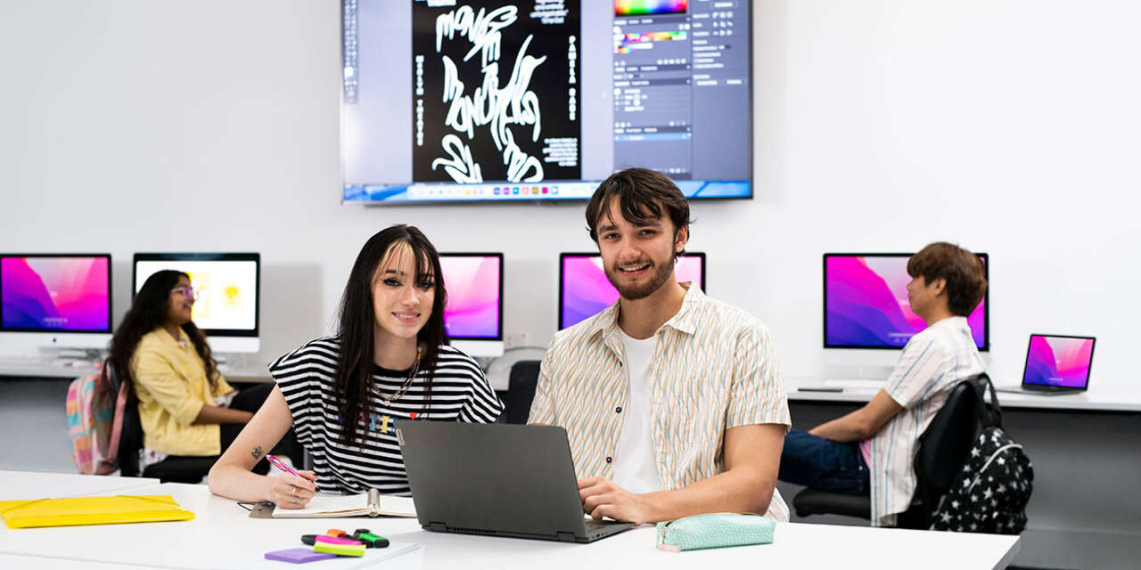 Two students sitting at computer smiling at camera