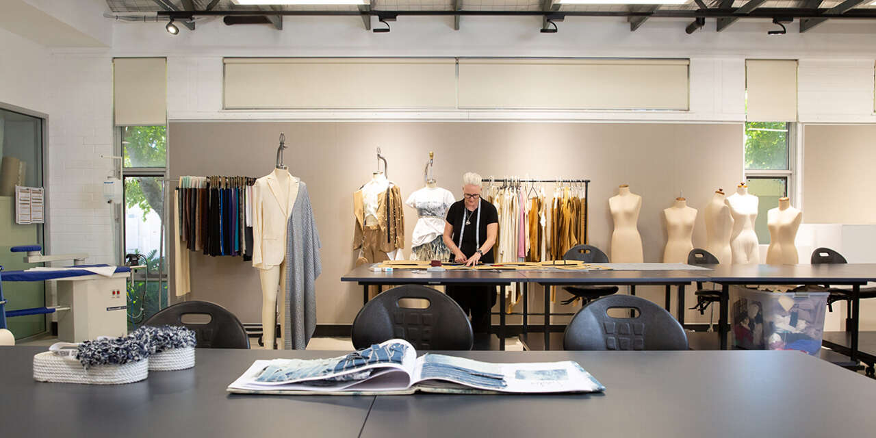 A person working on textiles surrounded by mannequins and garments.