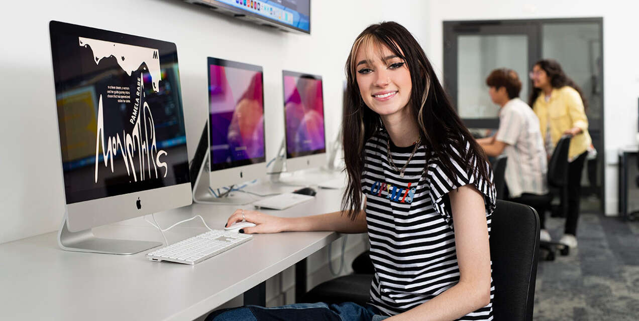 A woman sitting at a computer smiling at the camera.