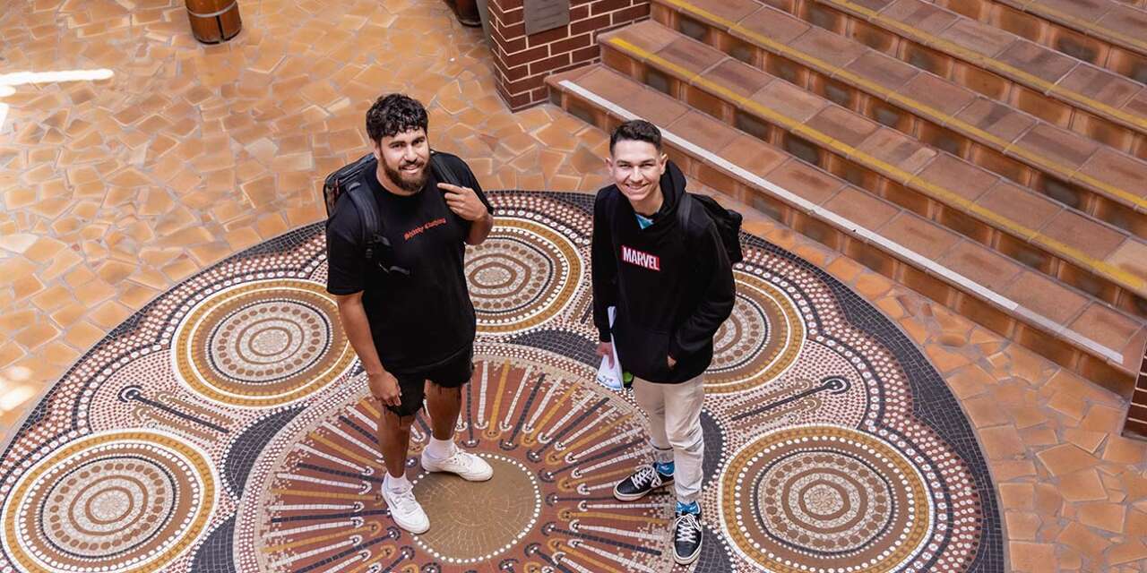 Two students standing near Indigenous artwork