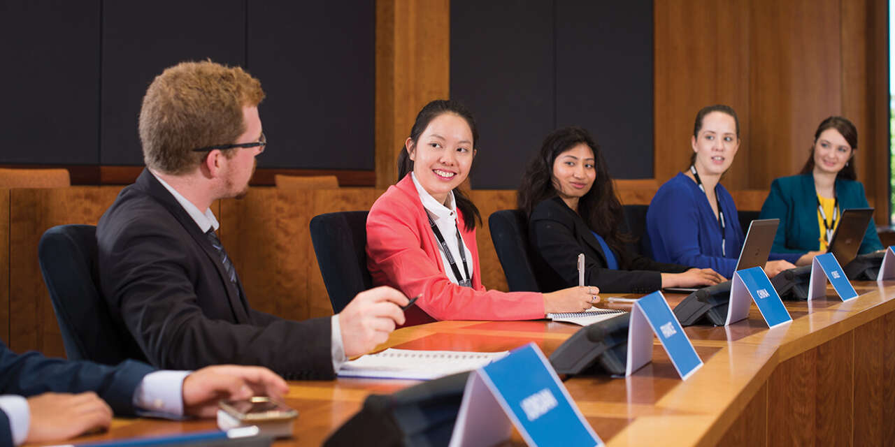 Group of students sitting at behind a long court like desk with name plaques in front them.