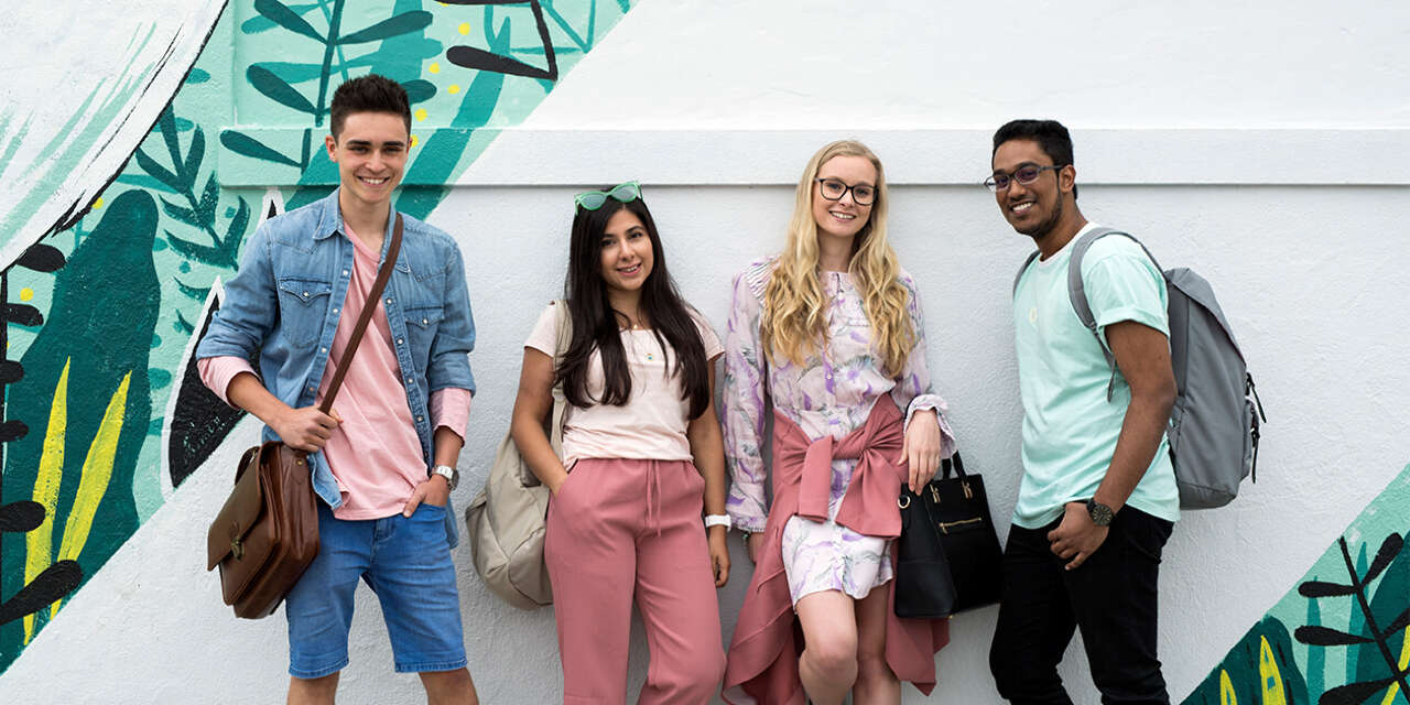 Four students standing in front of a wall