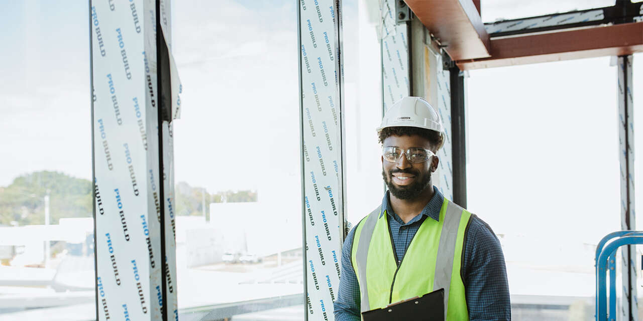 Man holding a clipboard in a high vis jacket on a property construction site