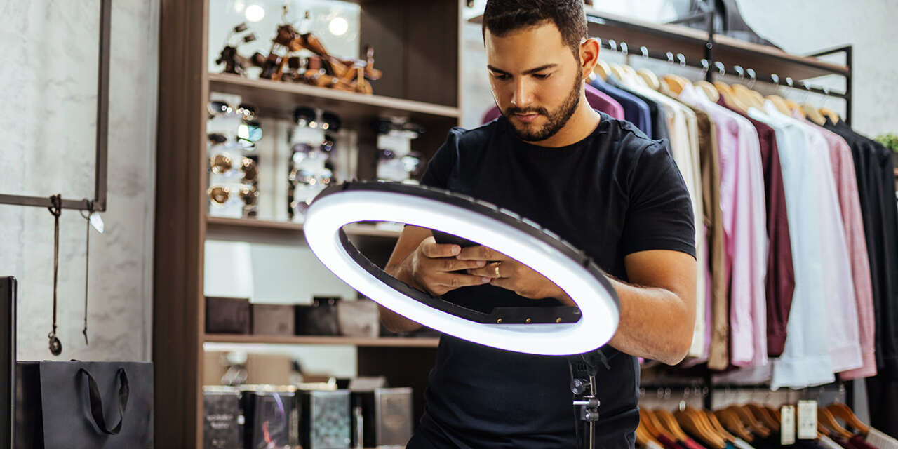 Man looks at ring light with clothes in background.
