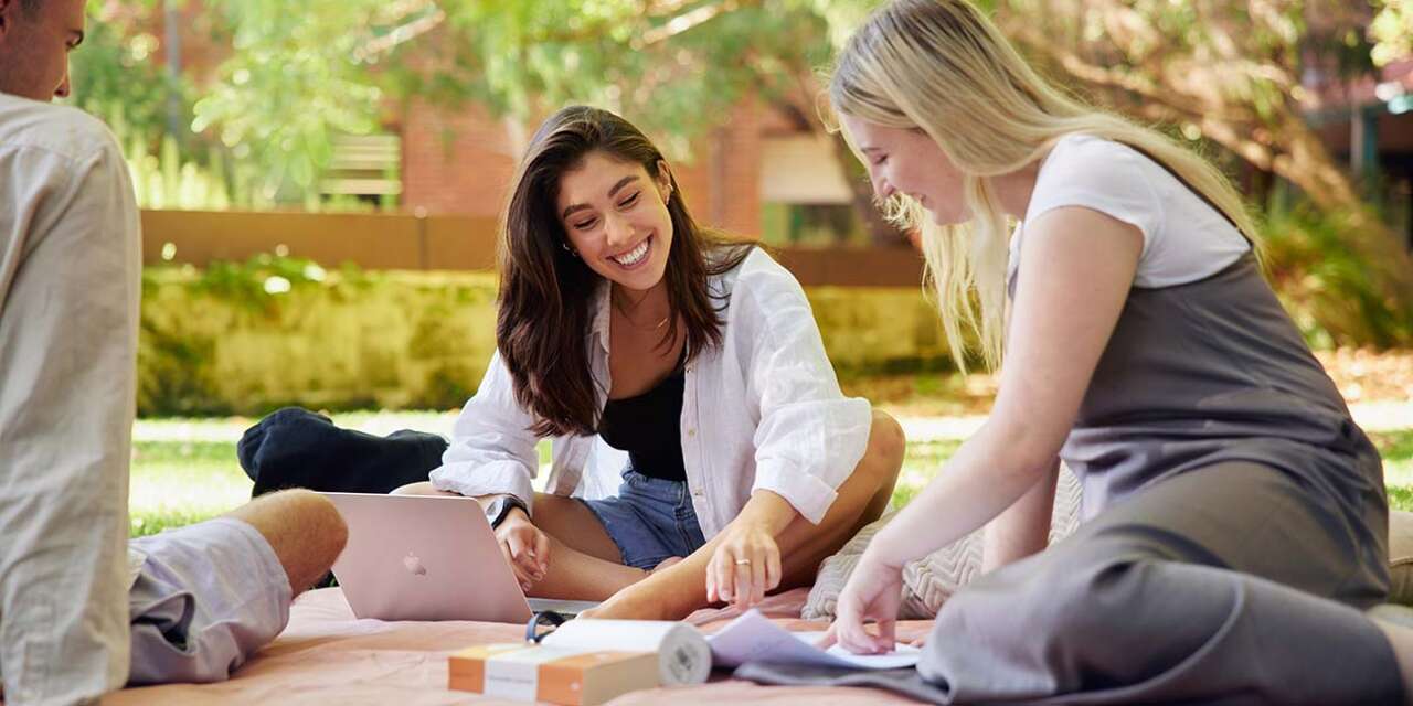 Students sitting outside on a grassed area at Curtin campus