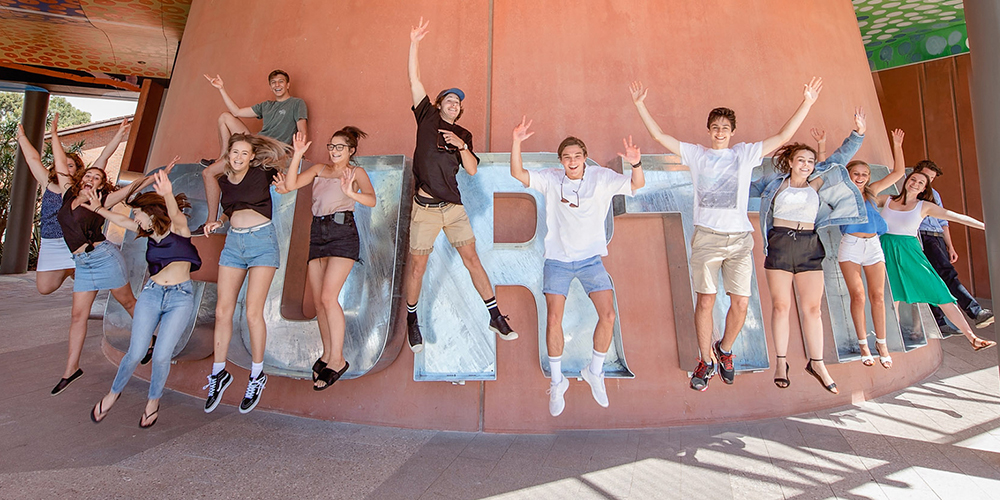 Students leaping in air and smiling in front of Curtin cookie cutter sculpture - play video