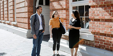 Two business women and a business man standing out the front of the Curtin Business School