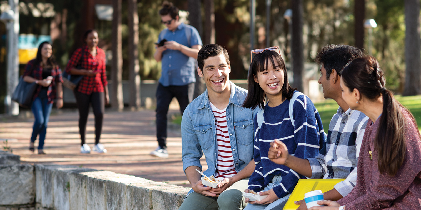 A group of students sitting on a wall, all looking at each other and smiling