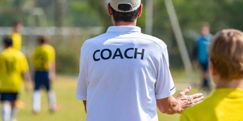 Football coach wearing a white shirt which reads 'coach'
