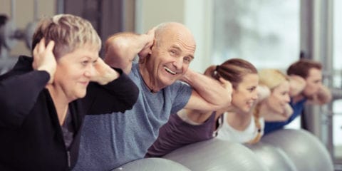 Elderly man exercising on a fitness ball in a group.
