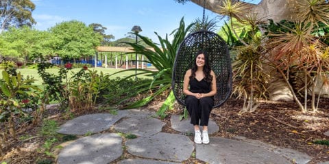 A Curtin student sitting in a hanging chair in a green garden