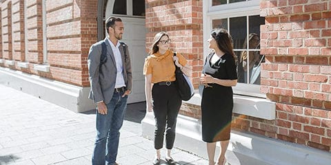 One male and two female students standing out the front of a building smiling