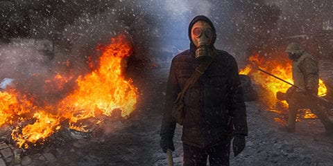 Radical Protestant in the mask represents the protesters against the authorities among the burning of the capital of the European quarter. Burning rubber tires wheel of fire smoke soot street fighting